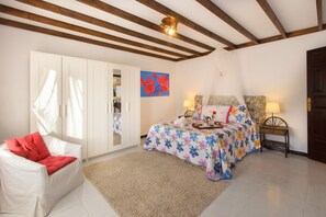 Une chambre à coucher avec un lit, une chaise blanche, une armoire et un tableau accroché au mur.