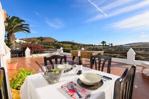 Un espace de restauration en plein air avec une table dressée pour deux personnes, entourée de chaises, d’une plante en pot et offrant une vue sur le paysage.