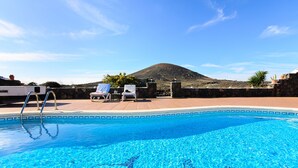 Une piscine à l’eau d’un bleu cristallin, un mur de pierre et une montagne en arrière-plan.