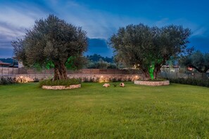 A well-maintained garden with two large trees, a stone wall, and a grassy lawn.