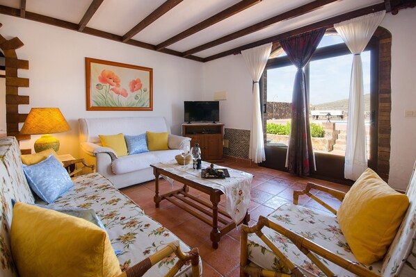 A living room with a sofa, chairs, a table, a TV, and a painting on the wall. - Clara Suite 2: Large Pool, Spectacular Views, Terrace & Garden in Lanzarote (Masdache)