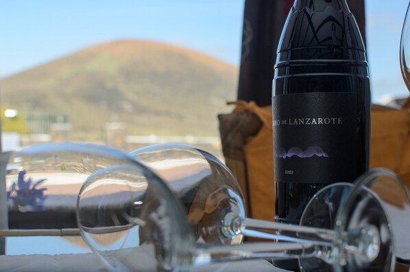 A bottle of wine with a label, glasses, and a mountain in the background. - Clara Suite 2: Large Pool, Spectacular Views, Terrace & Garden in Lanzarote (Masdache)