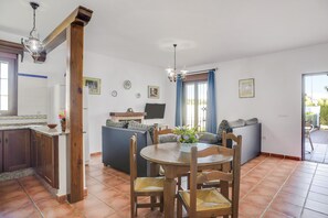 Un comedor con una mesa y sillas de madera, una cocina con armarios de madera y una sala de estar con sofá y televisor.