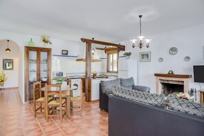 Una sala de estar con sofá, una mesa de comedor con sillas, una zona de cocina y una chimenea.