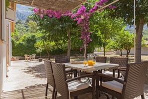 Un patio al aire libre con mobiliario de mimbre, una mesa con bebidas y vistas a un jardín exuberante.