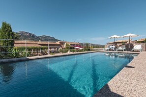 Una piscina con sillas de descanso y sombrillas, rodeada de edificios y montañas.