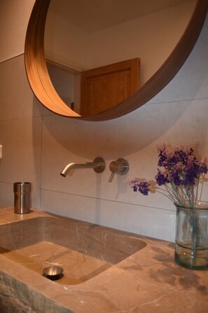Un baño con un espejo redondo, un lavabo con grifo y un florero con flores.