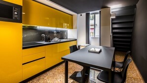 A compact kitchen with yellow cabinets, a black countertop, and a dining area with a table and chairs. - 18 · Extreme design style - Bologna Downtown Apartment (Bologna)