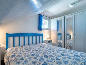 Une chambre à coucher avec un lit, une table de chevet, une fenêtre avec des rideaux bleus et une armoire.