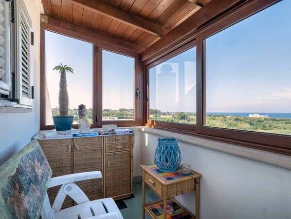 A balcony with a view of the sea, a potted plant, a wicker table, and a chair.