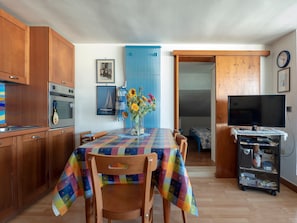 Une cuisine avec des meubles en bois, un fourneau et une table à manger recouverte d’une nappe colorée.
