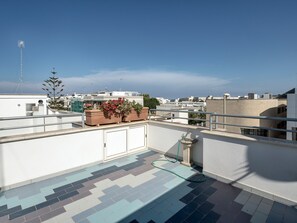 A rooftop terrace with a tiled floor, potted plants, and a view of the cityscape.
