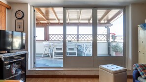 A living room with a television, a sofa, a small table, and a sliding glass door leading to an outdoor patio with chairs and a table.