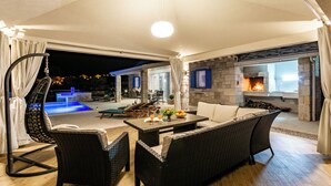 An outdoor living area with wicker furniture, a stone fireplace, and a pool. - Villa Blue Sky (Bol)