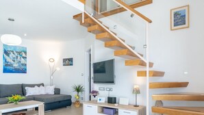 A modern living room with a staircase, a sofa, a coffee table, a TV, and a painting. - Villa Blue Sky (Bol)