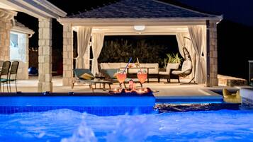 A pool area with a hot tub, lounge chairs, and a covered seating area with drinks.