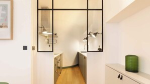 A narrow hallway with a mirrored wall, a green chair, and a cabinet with a green container.