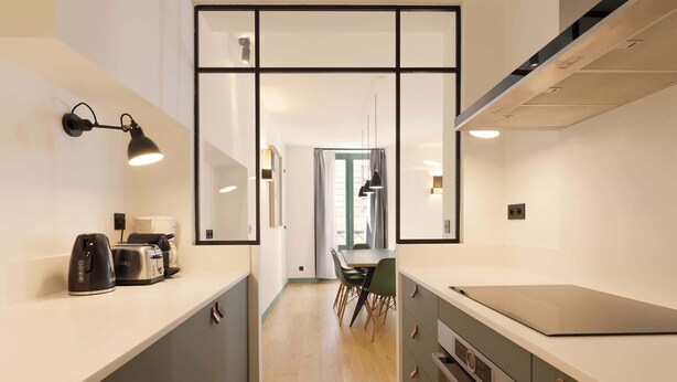 A narrow kitchen with a countertop, a stove, and a dining area with chairs.
