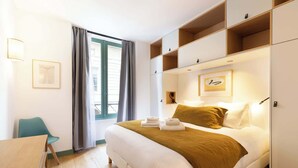 A hotel room with a bed, a desk, a chair, and a window with curtains.