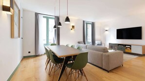 A modern living room with a dining area, large windows, a flat-screen TV, and a sofa.
