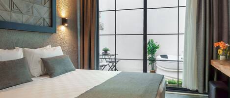 Una habitación de hotel moderna con una cama grande, vistas al exterior y un pequeño balcón.