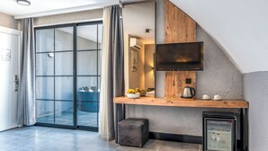 Una sala moderna con puerta corrediza de vidrio, estante de madera con televisor, refrigerador pequeño y una zona de estar con banco.