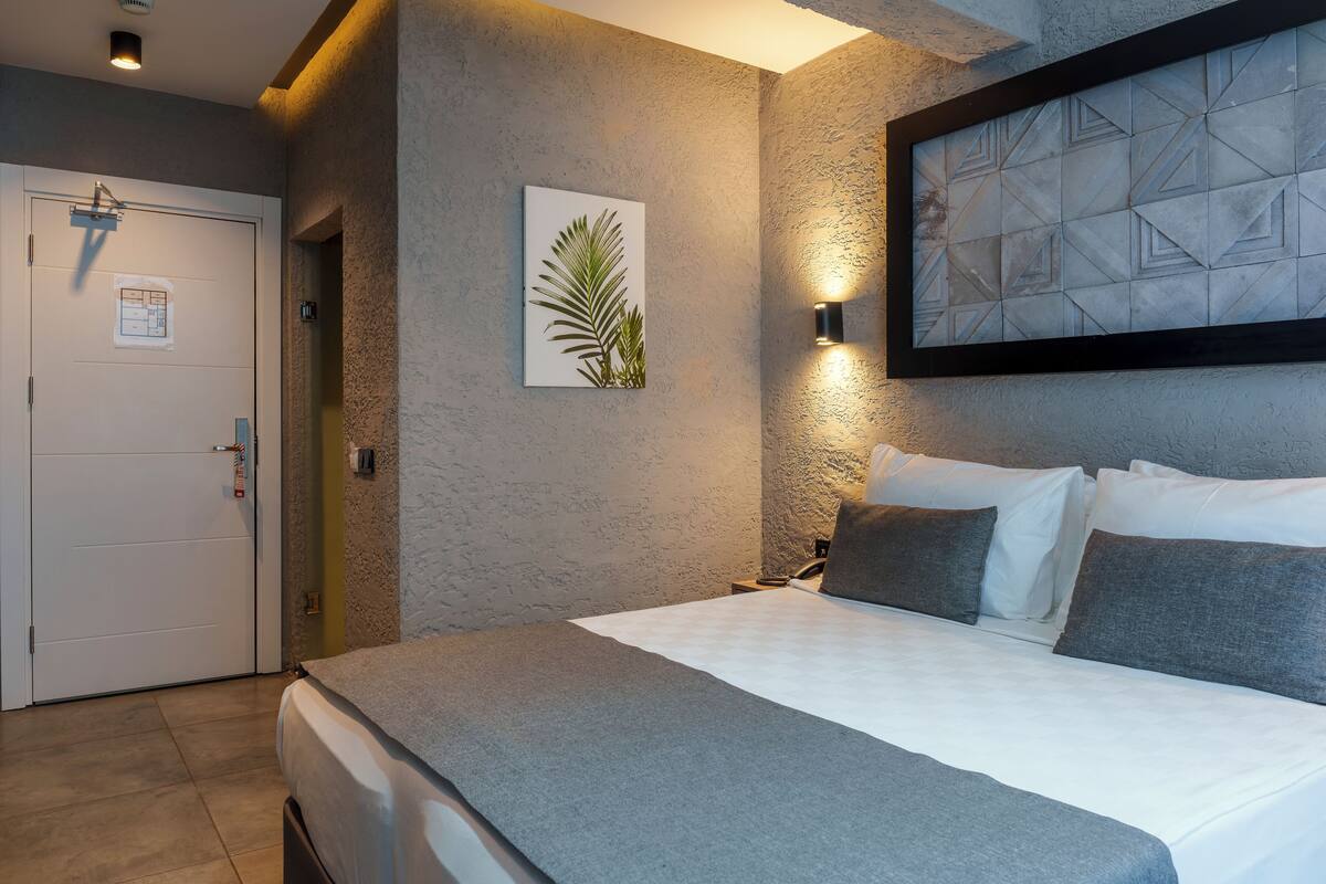 Moderni hotellihuone, jossa on suuri sänky, seinään kiinnitetty valaisin ja turvalukolla varustettu ovi.