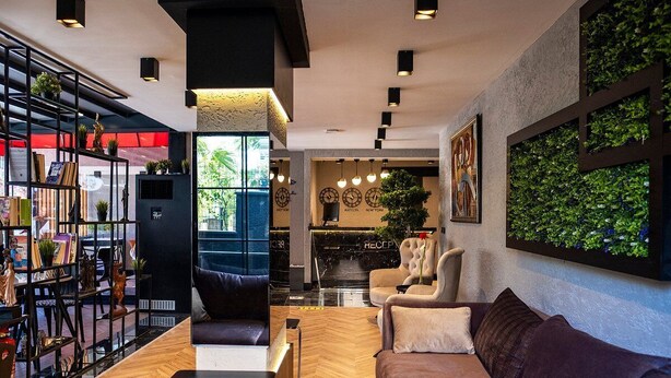 Un moderno vestíbulo de hotel con suelo de madera, una recepción, un sofá, una estantería y una pared cubierta de vegetación.