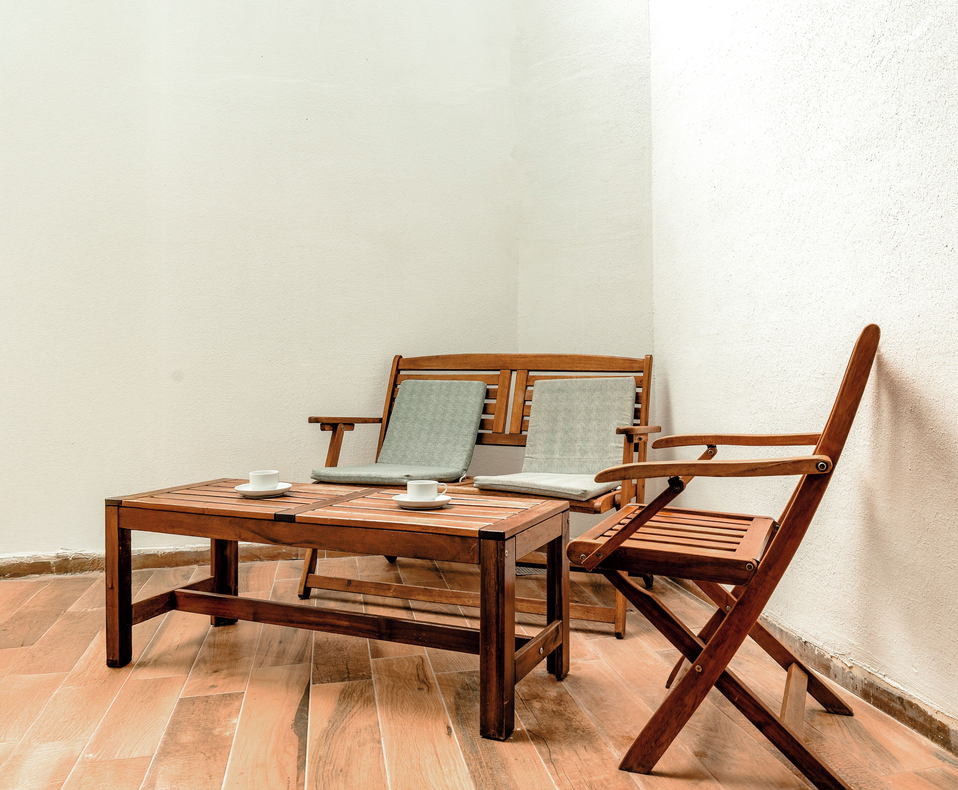 A corner of a room with a wooden table and two wooden chairs, one with a cushion.