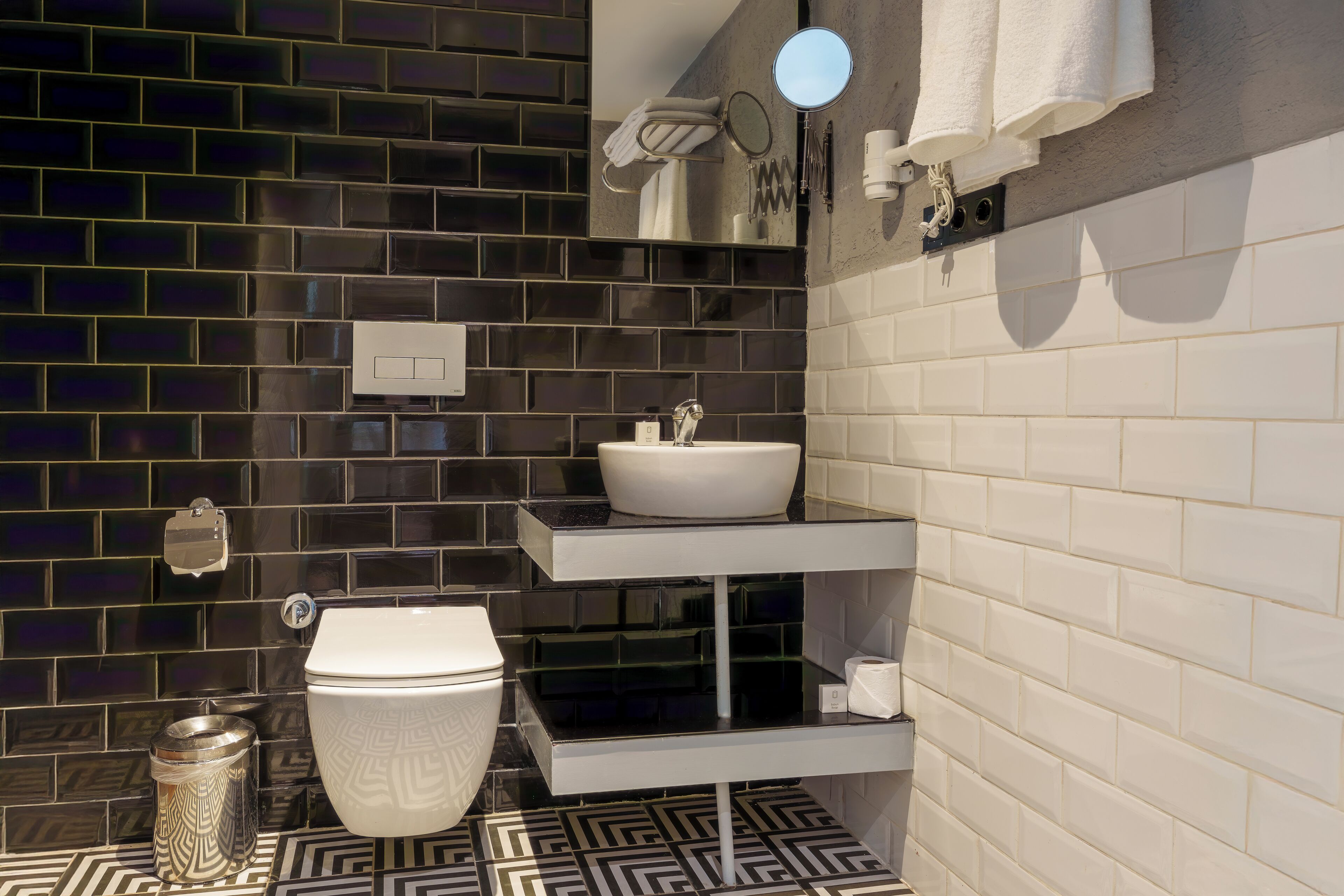 A modern bathroom with a black and white tiled backsplash, a white sink, and a toilet.