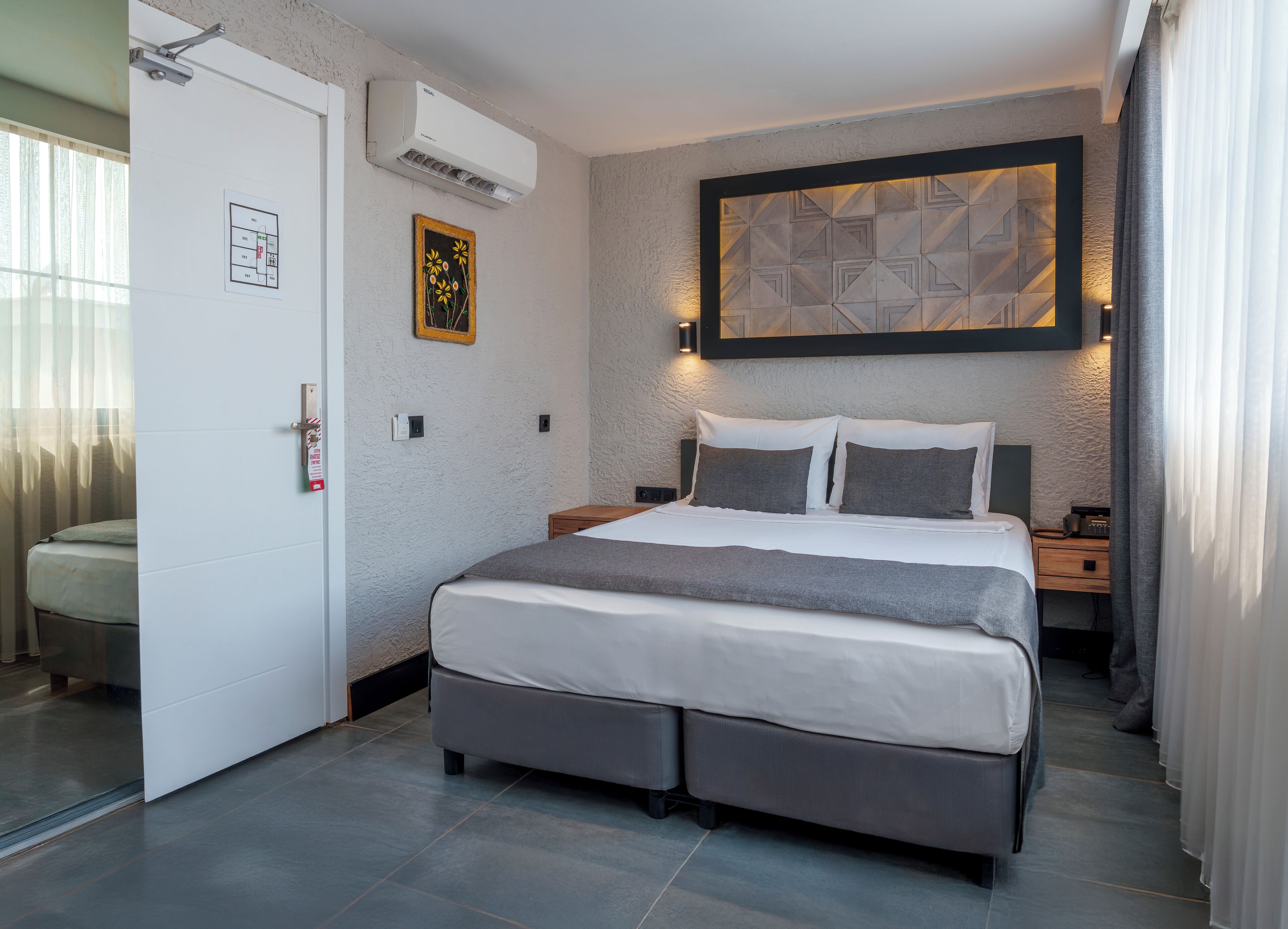 Ein modernes Hotelzimmer mit einem großen Bett, Nachttischen, einer Klimaanlage und einem dekorativen Wandbild.
