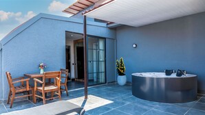 Un patio moderno al aire libre con una mesa y sillas de madera, un jacuzzi y una planta en maceta.