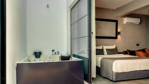 Un baño moderno con una bañera grande, ducha e inodoro. La habitación cuenta con una puerta corredera de vidrio que da a un dormitorio con cama y mesita de noche.