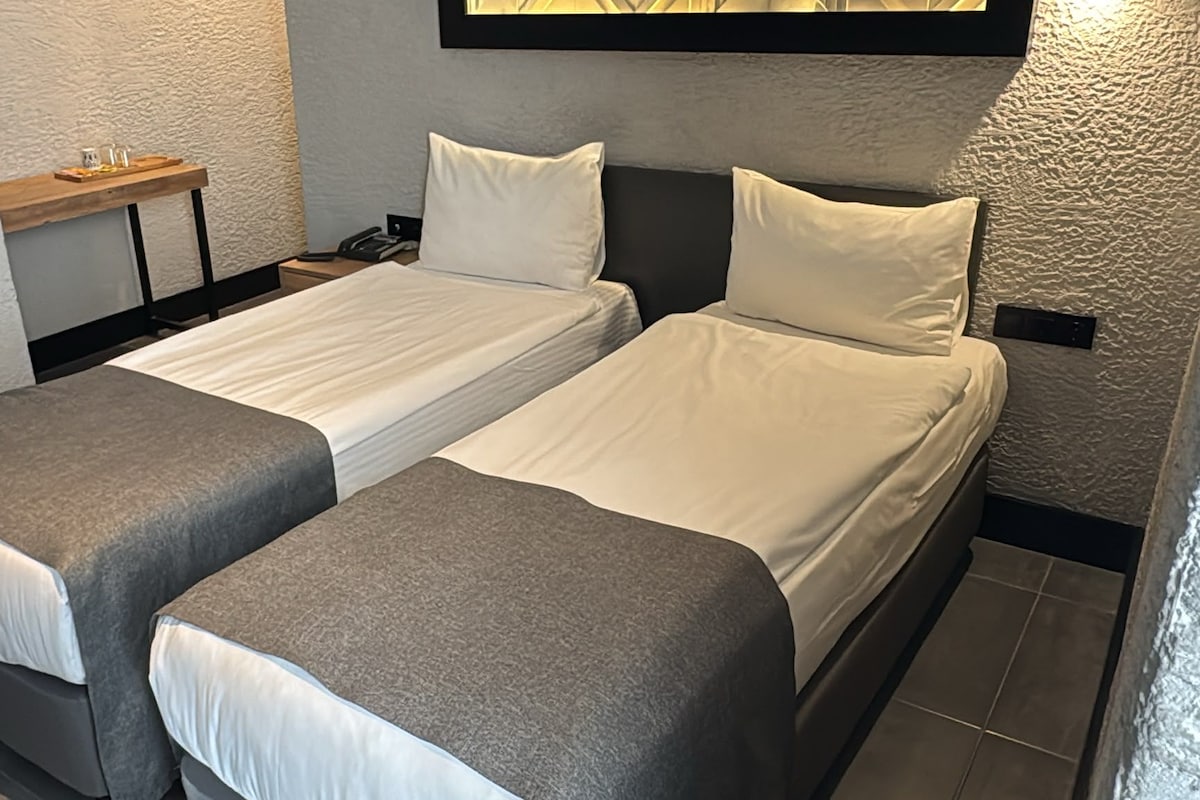 A twin room with two single beds, a small table, and a wall-mounted shelf.