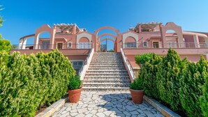 A building with a central staircase leading to an arched entrance, surrounded by potted plants. - Villa Leo 1 , Dassia , Corfu (Corfu)