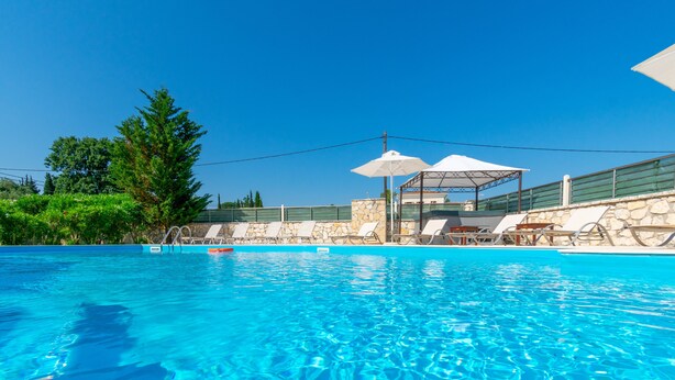 Piscina azul cristalina con sillas de descanso y sombrillas, rodeada de muros de piedra y follaje.