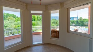Amplia habitación con ventanas grandes que ofrecen vistas a un balcón y vegetación.