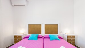 A double room with two beds, wooden headboards, bedside tables with drawers, and an air conditioning unit on the wall.