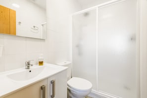 Ein Badezimmer mit einem weißen Waschbecken, einem Spiegel, einem Holzschrank, einer Toilette und einer Duschkabine aus Glas.