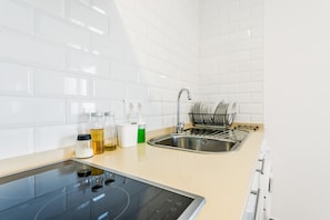 Una cucina moderna con piastrelle bianche, un lavello in acciaio inossidabile, un portascopi e un piano cottura a induzione integrato.