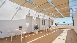 A spacious outdoor patio with white furniture, potted plants, and a tiled floor.