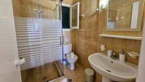 A bathroom with a glass-enclosed shower, a toilet, a sink, and a mirror.