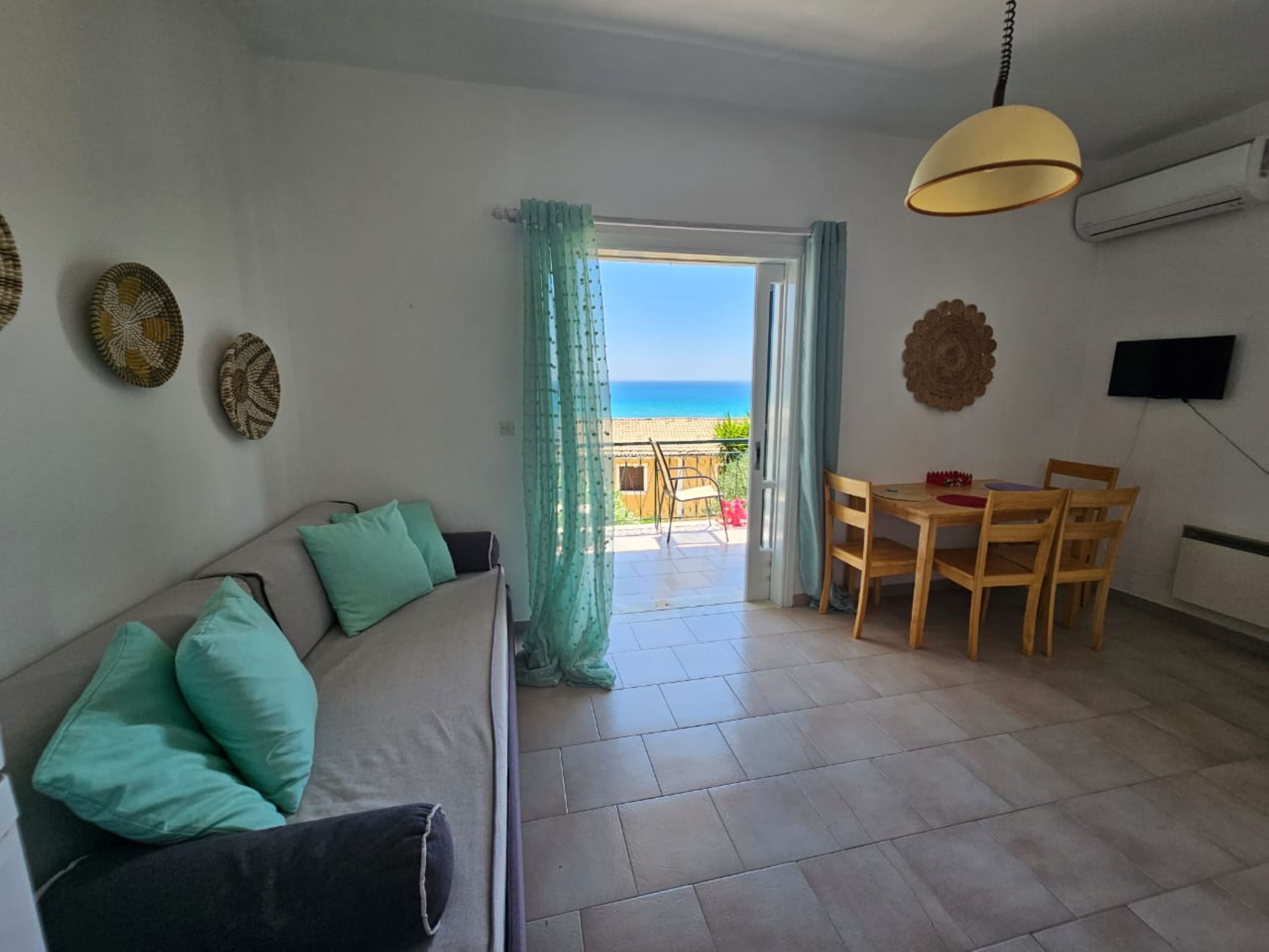Una habitación con sofá, mesa de comedor, sillas, televisor y vista al mar.