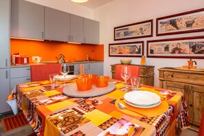 Un coin repas avec une table dressée pour quatre personnes, une cuisine en arrière-plan et des œuvres d’art accrochées aux murs.