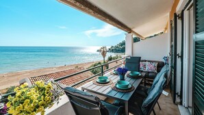 Varanda com vista para o mar, mesa com pratos azuis e um vaso de flores, e um sofá com almofadas.
