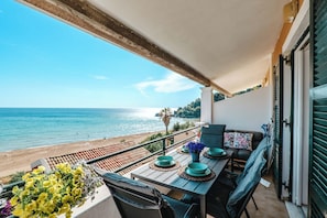 Un balcón con vista al mar, una mesa con platos azules y un jarrón de flores, y un sofá con cojines.