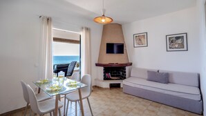 Uma sala de jantar com mesa de vidro, cadeiras, um sofá, uma TV e uma lareira.