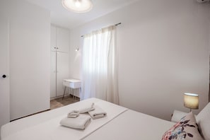Una habitación de hotel con cama, escritorio, silla, lámpara y armario.