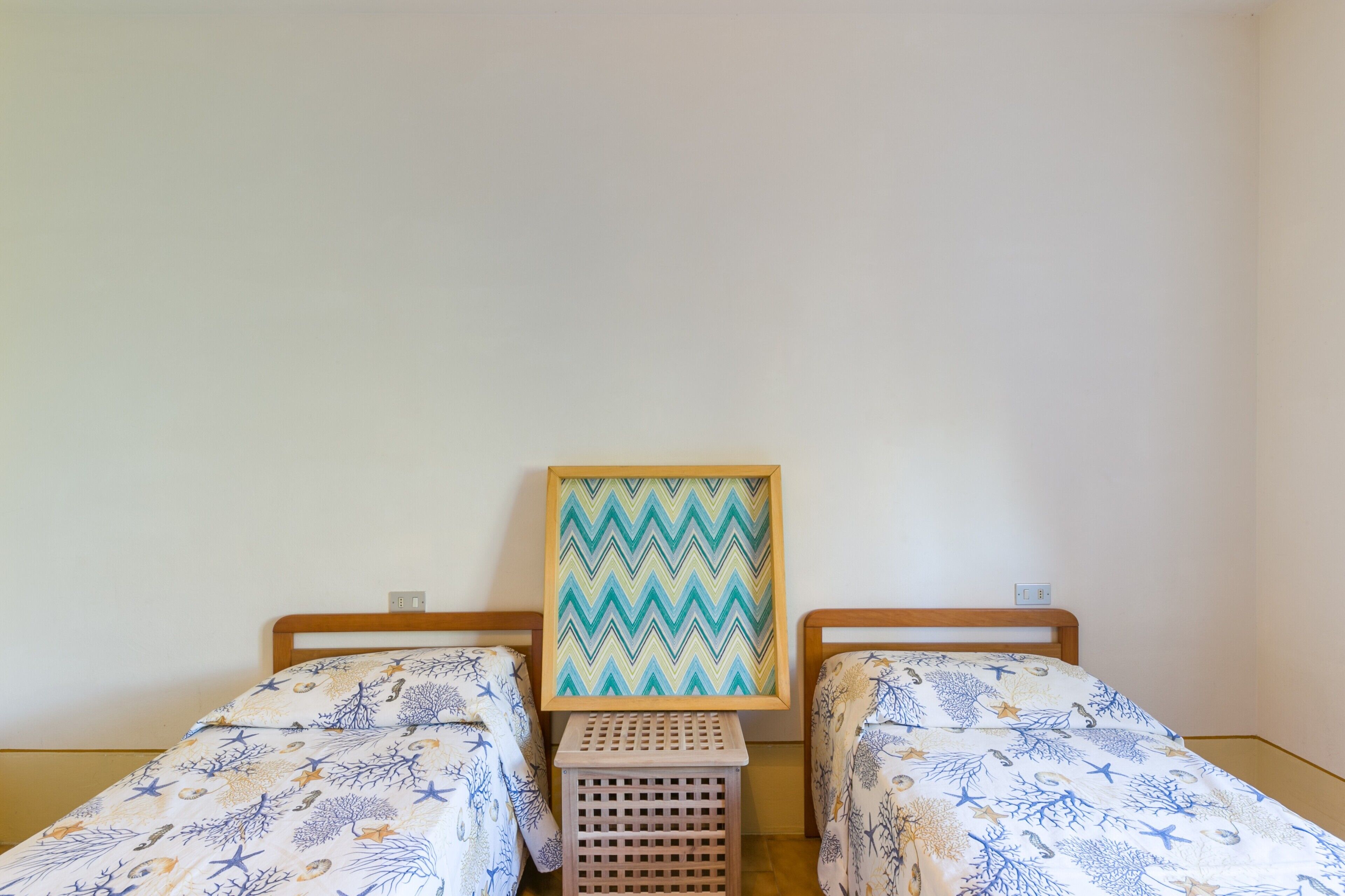 A room with two single beds, a wooden headboard, a small wooden stool, and a framed picture on the wall.