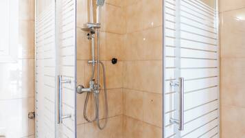 A glass-enclosed shower with a handheld showerhead, a wall-mounted faucet, and a control panel.